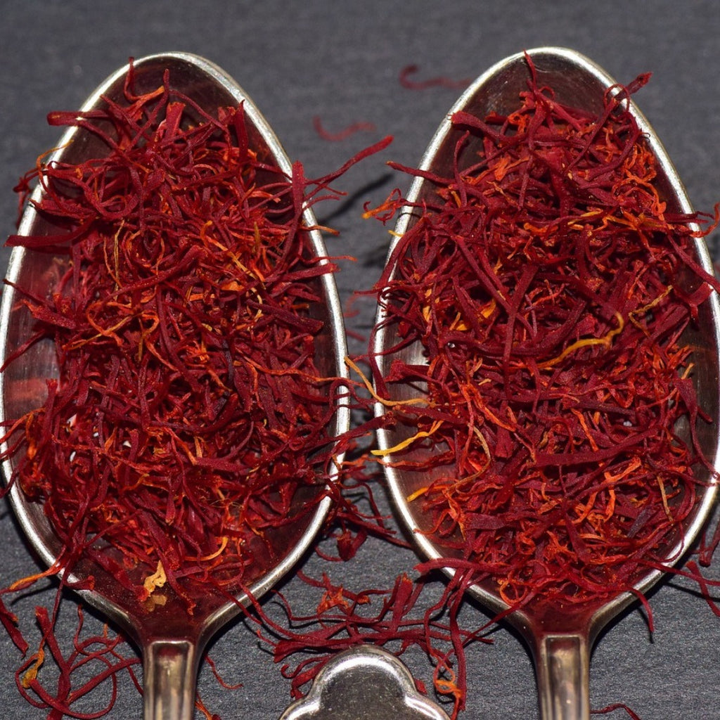 Two spoons filled with red saffron threads on a dark background