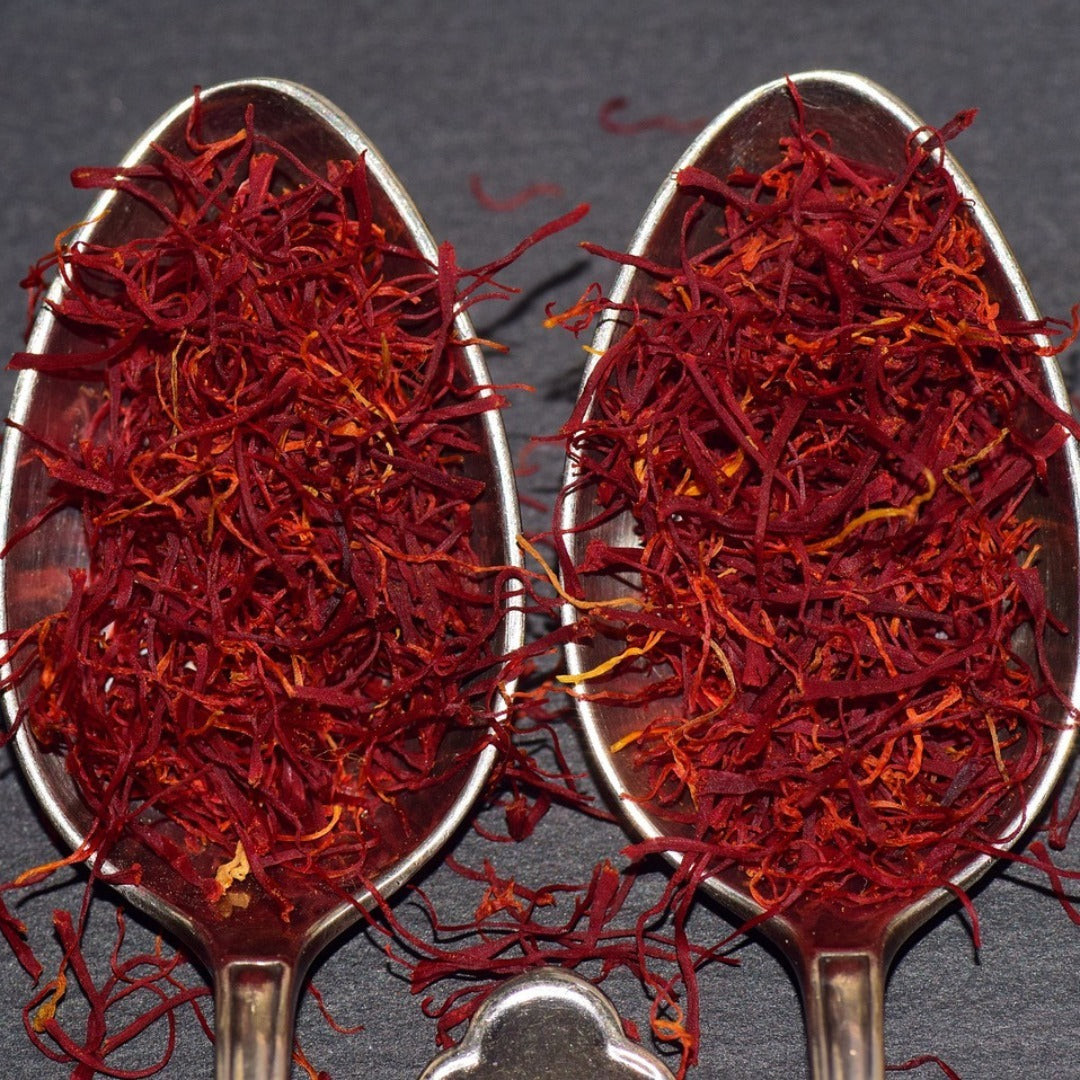 Two spoons filled with red saffron threads on a dark background