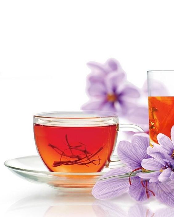 Two glass cups filled with red saffron tea, surrounded by fresh saffron flowers on a white background